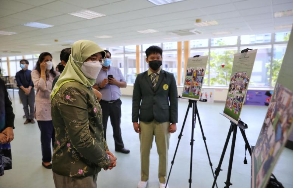 People wearing face masks stand in an indoor hall viewing photo displays mounted on tripod easels.